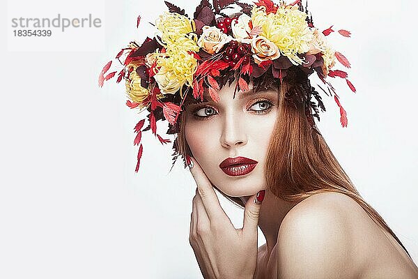 Schönes Mädchen mit hellem Herbstkranz aus Blättern und Blumen. Schönes Gesicht. Bild im Studio auf einem weißen Hintergrund genommen