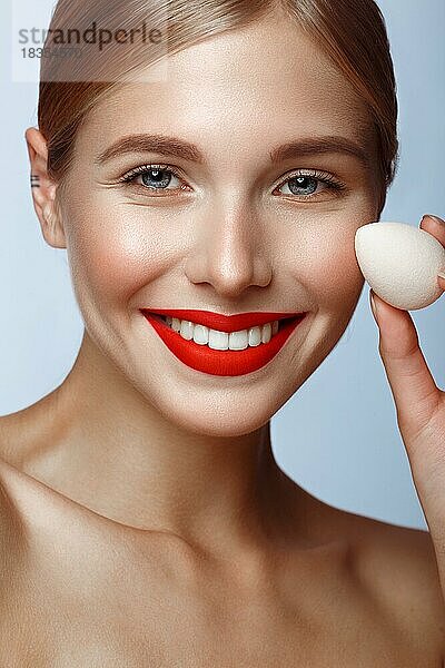 Schönes Mädchen mit roten Lippen und klassischen Make-up mit Stiftung Schwamm in der Hand. Schönes Gesicht. Foto im Studio aufgenommen