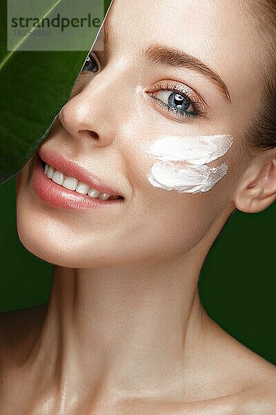 Schönes frisches Mädchen mit Kosmetikcreme auf dem Gesicht  natürliches Make-up und grüne Blätter. Schönes Gesicht. Foto im Studio aufgenommen