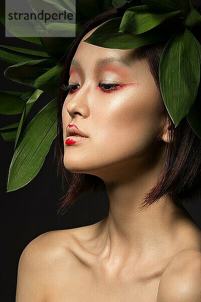 Schönes asiatisches Mädchen mit einem hellen Make-up Kunst in grünen Blättern. Schönes Gesicht. Kreatives Bild. Bild im Studio aufgenommen