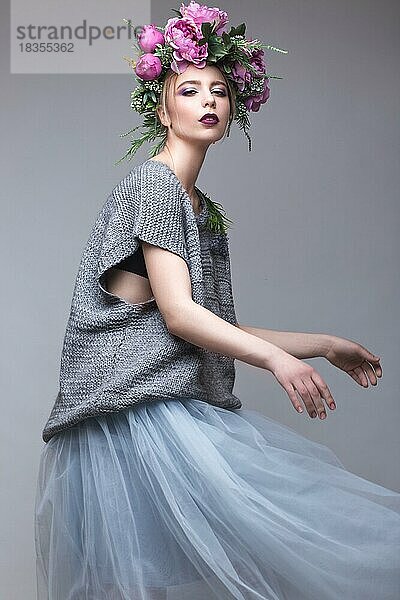 Schönes Mädchen mit Blumen auf dem Kopf in Mode Kleidung posiert gegen den Hintergrund im Studio. Schönheit Stil