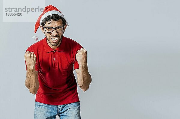 Mann mit Bart und Weihnachtsmütze blickt wütend in die Kamera  isoliert. Wütender Weihnachtsmann schaut in die Kamera. Menschen in Weihnachtsmützen wütend und wütend Blick in die Kamera