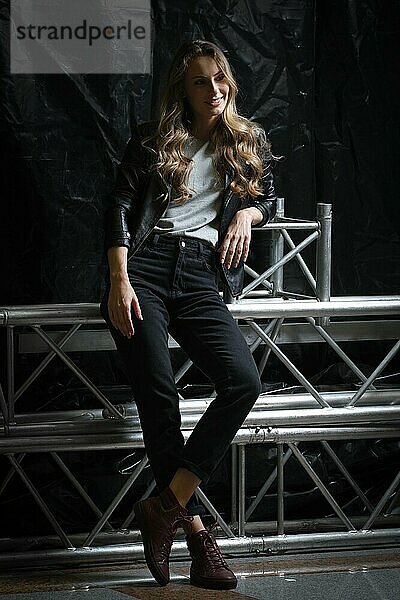 Schönes Mädchen mit langen lockigen Haaren in schwarzer Lederjacke  T-Shirt und Jeans