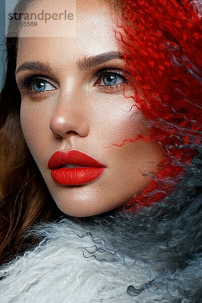 Schöne Frau mit klassischem Urlaubs-Make-up  roten Lippen  Locken im mehrfarbigen Lamamantel. Schönes Gesicht. Foto im Studio aufgenommen