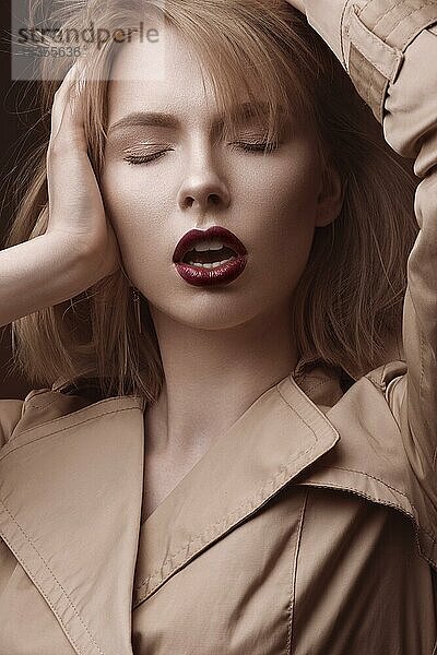 Schöne blonde Frau in einem hellen Mantel und dunklen Lippen  zeigt verschiedene Posen. Schönes Gesicht. Bild im Studio aufgenommen