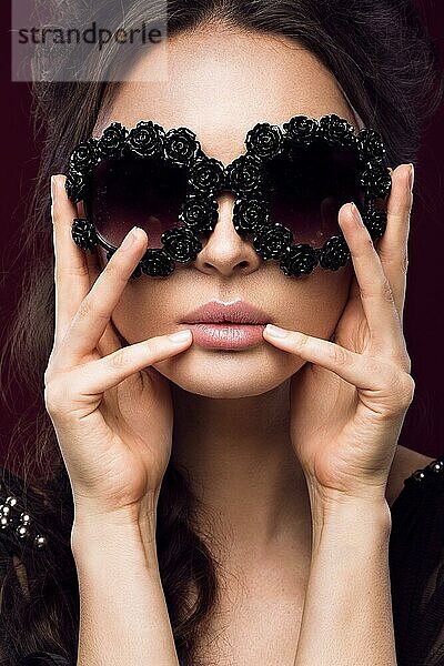 Schönes Mädchen mit dunkler Sonnenbrille  mit Locken und Abend-Make-up. Schönes Gesicht. Bild im Studio auf einem schwarzen Hintergrund genommen