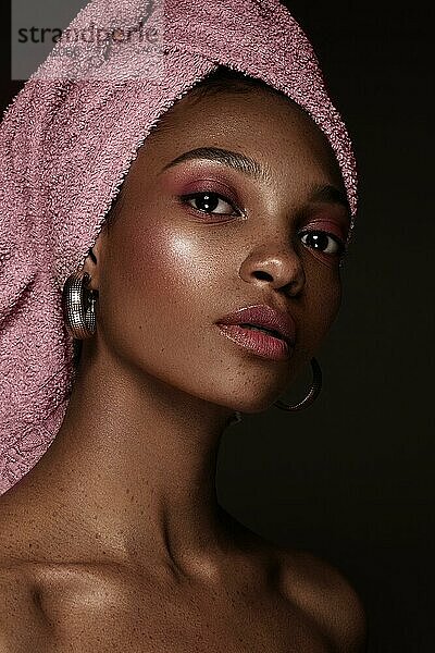 Schöne schwarze Frau mit einem rosa Handtuch auf dem Kopf und klassischem Make-up. Schönes Gesicht. Foto im Studio aufgenommen