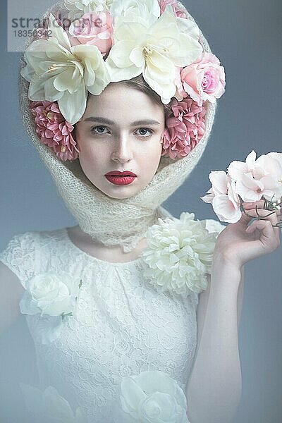 Schönes Mädchen mit einem Kopftuch im russischen Stil  mit großen Blumen auf dem Kopf und roten Lippen. Schönheit Gesicht. Bild im Studio auf einem grauen Hintergrund genommen