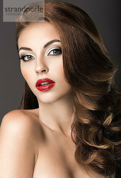 Schöne Frau mit Abend-Make-up  roten Lippen und Locken. Schönes Gesicht. Bild im Studio auf einem grauen Hintergrund genommen