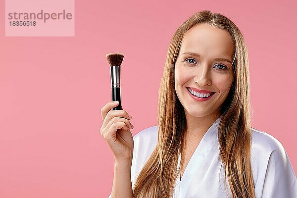 Schönes Mädchen mit Make-up-Pinsel in der Hand über rosa Hintergrund