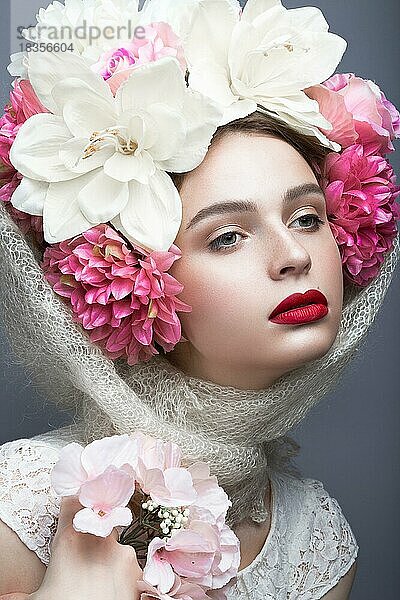 Schönes Mädchen mit einem Kopftuch im russischen Stil  mit großen Blumen auf dem Kopf und roten Lippen. Schönheit Gesicht. Bild im Studio auf einem grauen Hintergrund genommen