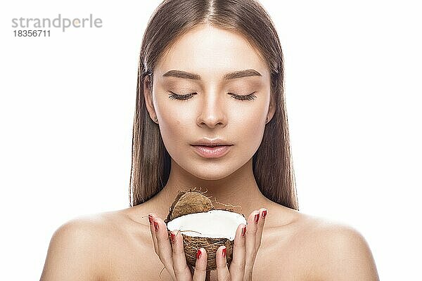 Schönes junges Mädchen mit einem leichten natürlichen Make-up und perfekter Haut mit Kokosnuss in der Hand. Schönes Gesicht. Bild im Studio auf einem weißen Hintergrund aufgenommen