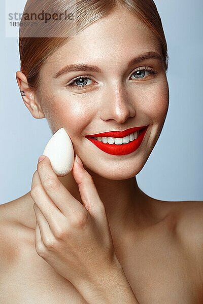 Schönes Mädchen mit roten Lippen und klassischen Make-up mit Stiftung Schwamm in der Hand. Schönes Gesicht. Foto im Studio aufgenommen