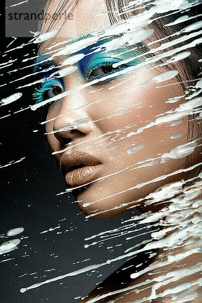 Schönes asiatisches Mädchen mit hellblauem Make-up hinter Glas mit Wachstropfen. Schönes Gesicht. Bild im Studio auf einem schwarzen Hintergrund genommen