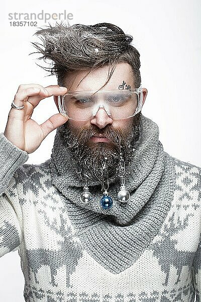 Lustiger bärtiger Mann in einem Neujahrsbild mit Schnee und Dekorationen auf seinem Bart. Fest der Weihnacht. Fotos im Studio aufgenommen