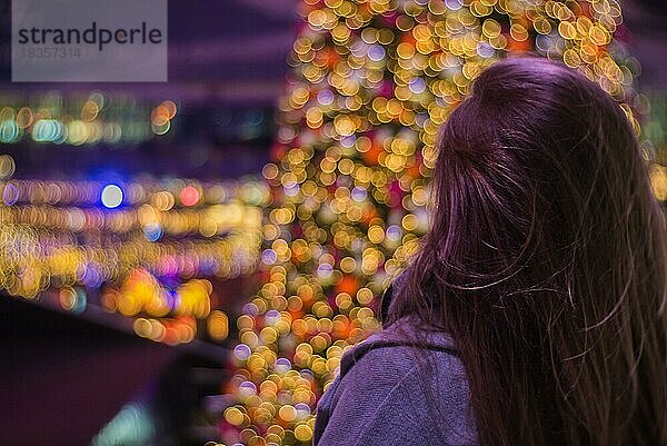 Mädchen vor einem unscharfen Blick auf einen Weihnachtsbaum mit Lichterketten