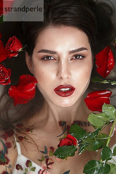 Schönes Mädchen mit klassischem Make-up und roten Lippen im Badezimmer mit Blumen. Schönes Gesicht. Foto im Studio aufgenommen