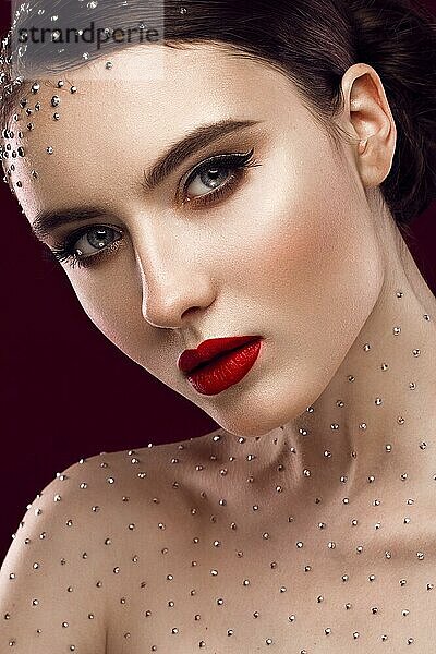 Porträt eines schönen Mädchens mit einem hellen Make-up  roten Lippen und Kristallen auf dem Körper. Die Schönheit des Gesichts. Fotos im Studio geschossen