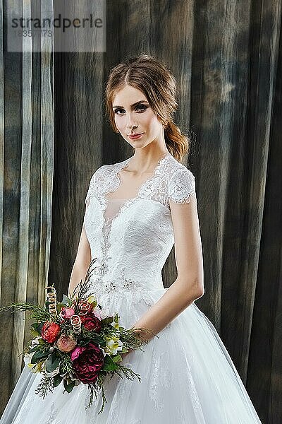 Porträt einer hübschen Braut im Hochzeitskleid mit Blumen in den Händen