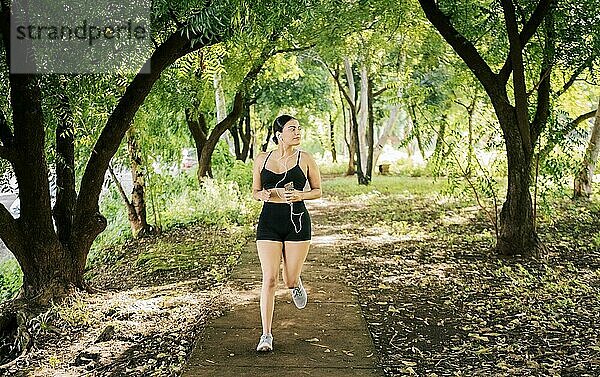 Lifestyle einer sportlichen jungen Frau  die in einem von Bäumen umgebenen Park läuft. Gesunder Lebensstil Konzept  Sportliche junge Frau läuft in einem Park. Ein Mädchen läuft in einem Park  während es Musik hört