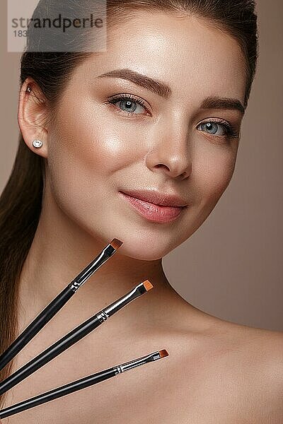 Schönes junges Mädchen mit natürlichen nackt Make-up mit kosmetischen Werkzeugen in den Händen. Schönes Gesicht. Foto im Studio aufgenommen