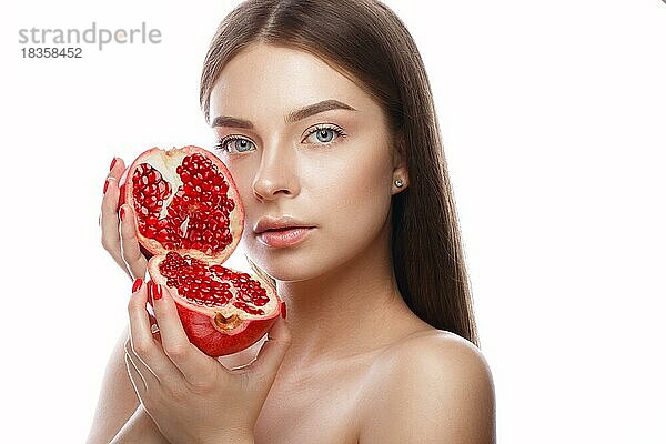 Schönes junges Mädchen mit einem leichten natürlichen Make-up und perfekter Haut mit Granatapfel in der Hand. Schönes Gesicht. Bild im Studio auf einem weißen Hintergrund aufgenommen