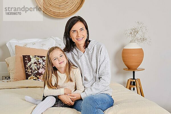 Lifestyle-Foto von Mutter und Tochter  die zu Hause auf dem Bett sitzen