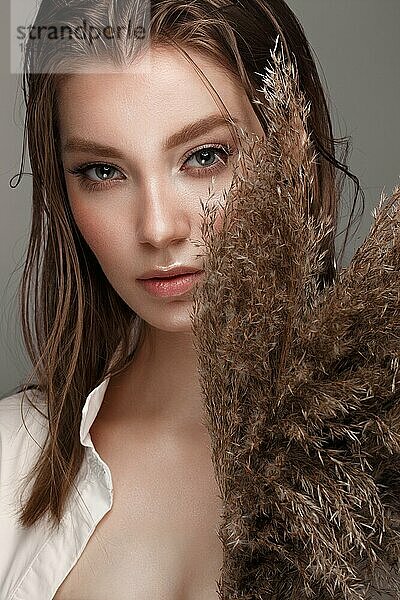 Schöne Frau mit klassischem Nackt-Make-up  heller Frisur und Trockenblumen. Schönes Gesicht. Foto im Studio aufgenommen