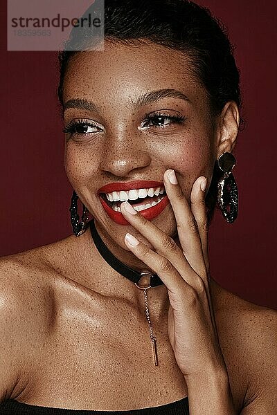 Schöne schwarze Frau mit einem Lächeln und roten Lippen und Sommersprossen. Schönes Gesicht. Foto im Studio aufgenommen