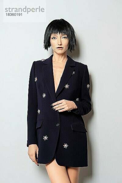 Modemodell mit schwarzem Bob Haarschnitt posiert in der Nähe der Wand in blauer Jacke mit Edelsteinen Dekor