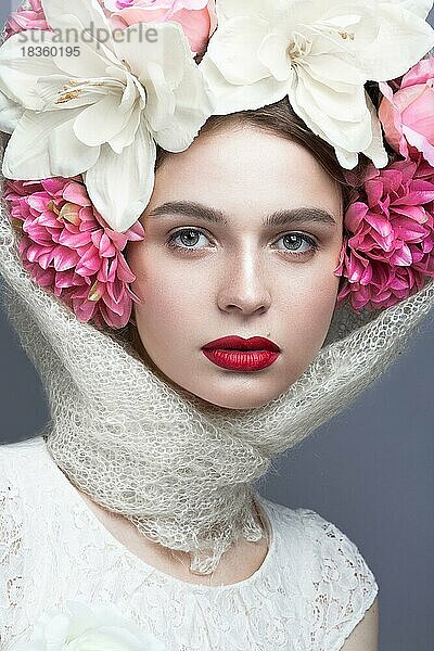 Schönes Mädchen mit einem Kopftuch im russischen Stil  mit großen Blumen auf dem Kopf und roten Lippen. Schönheit Gesicht. Bild im Studio auf einem grauen Hintergrund genommen