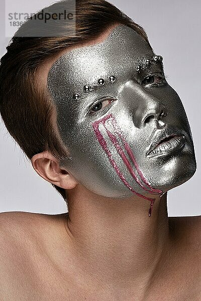 Junger Mann mit Kunst kreativen Kunst Make-up mit silberner Farbe auf seinem Gesicht. Schönheit Gesicht. Bild im Studio auf einem weißen Hintergrund genommen