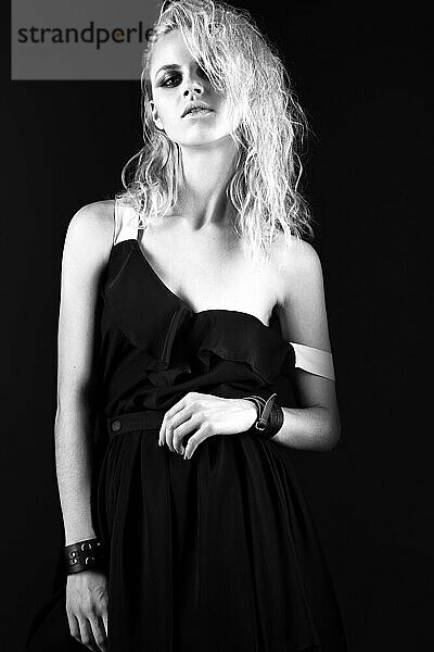 Gewagtes Mädchenmodell in schwarzem Seidenkleid im Rock-Stil  dunkles Make-up  nasse Haare und Armbänder an den Armen. Das Bild wurde im Studio aufgenommen. Schwarz-Weiß-Bild