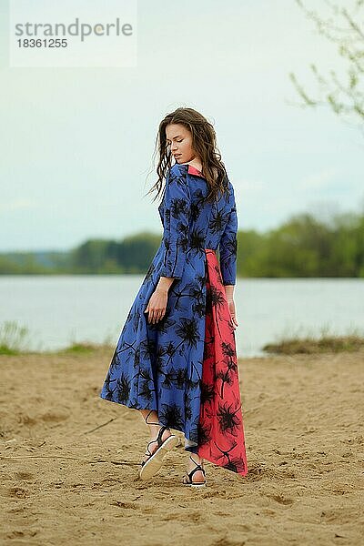 Porträt einer jungen Frau  die auf dem Sand spazieren geht. Romantische junge Frau in blauem Kleid mit Drucken