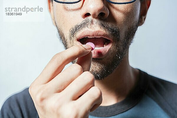 Person  die eine Pille einnimmt isoliert  Nahaufnahme eines jungen Mannes  der eine Pille in den Mund nimmt. Selbstmedikationskonzept  Mann nimmt eine Pille in den Mund isoliert  Nahaufnahme eines Mannes  der ein Aspirin nimmt