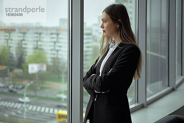 Hübsche Angestellte eines Bauunternehmens  die durch das Fenster ihres Büros auf der Baustelle schaut