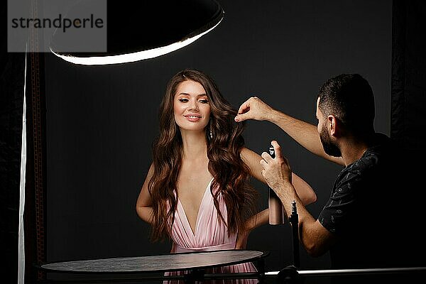 Friseur und schönes brünettes Mädchen mit perfekt gelocktem Haar und klassischem Make-up. Schönheit Gesicht. Bild im Studio aufgenommen