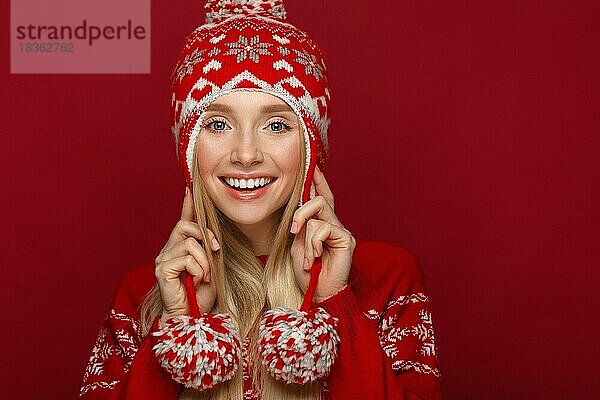 Schönes blondes Mädchen in einem Neujahrsbild in warmer Mütze und Pullover. Schönes Gesicht mit festlichem Make-up. Foto im Studio aufgenommen