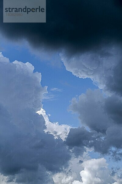 Lücke in weißen und grauen Wolken (Kumuluswolken) mit blauem Himmel an einem Regentag im Sommer