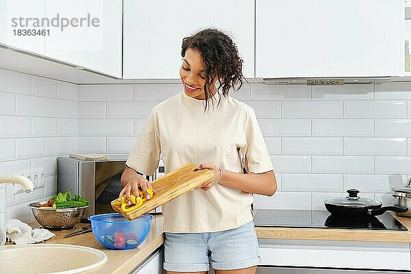 Hübsche afrikanische Frau kocht zu Hause. Hausfrau macht gesunden Vitamin-Salat aus frischem Gemüse