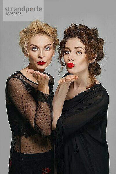 Zwei hübsche Models geben sich einen Luftkuss. Blonde und brünette Mädchen mit natürlichem Make-up und roten Lippen