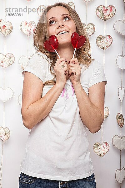 Valentinstag. Lustige schöne Frau hält Süßigkeiten in Form von Herzen. Schönheit Gesicht. Bild im Studio mit Dekorationen genommen