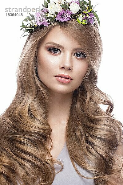Schönes blondes Mädchen mit sanftem Make-up  Locken und Blumen im Haar. Foto im Studio auf einem weißen Hintergrund aufgenommen