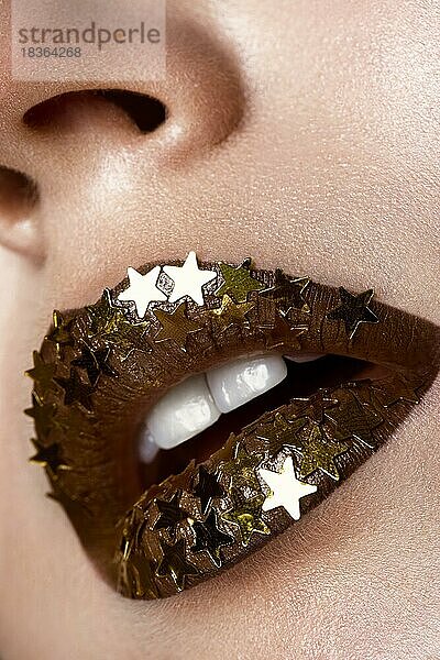 Schönes Mädchen mit einem goldenen glänzenden Sterne auf ihren Lippen. Schönes Gesicht. Foto im Studio aufgenommen