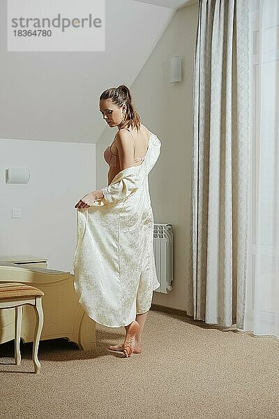 Hübsche junge Dame im Schlafzimmer aus Seide peignoir in der Nähe des Bettes vor dem Schlafengehen zu nehmen