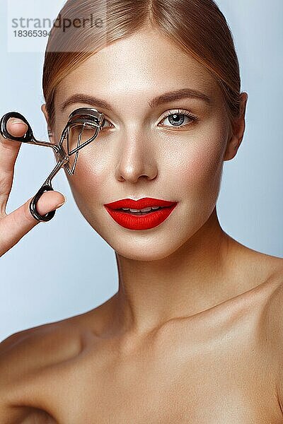 Schönes Mädchen mit roten Lippen und klassischem Make-up mit Lockenwickler in der Hand. Schönes Gesicht. Foto im Studio aufgenommen