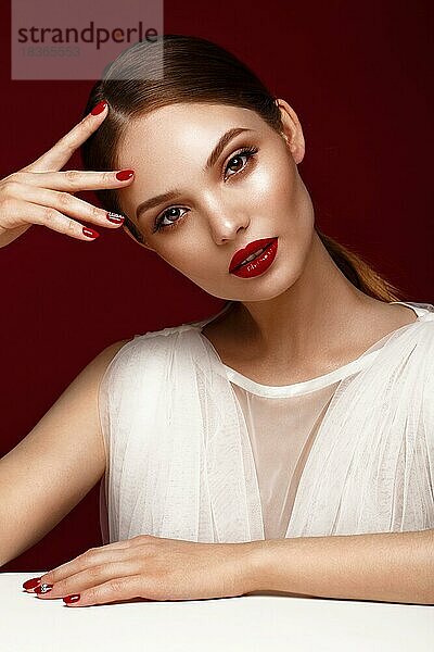 Schönes Mädchen im weißen Kleid mit klassischem Make-up und roter Maniküre. Schönes Gesicht. Foto im Studio aufgenommen