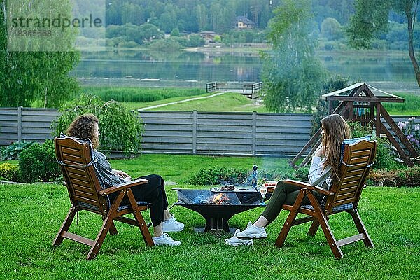 Zwei unerkennbare Frauen im Garten  die auf Stühlen sitzen und sich in der Nähe des Grills unterhalten