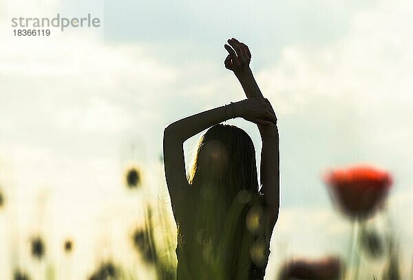 Silhouette eines Mädchens mit erhobenen Händen gegen die Sonne  Blumenfeld