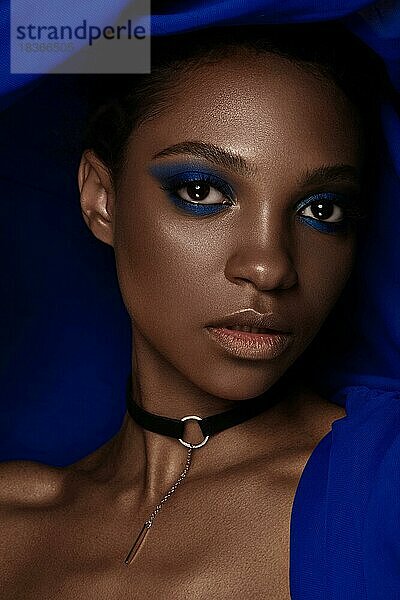 Schöne schwarze Frau mit blauem Stoff und klassischem Kunst-Make-up. Schönes Gesicht. Foto im Studio aufgenommen